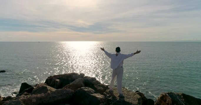 Mujer vestida de blanco adlib con brazos en cruz junto al mar