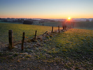 Frosty sunrise in the German city of Wipperfurth. A beautiful countryside landscape in the Bergisches Land region. Green pastures covered with frost in the rays of the rising sun.