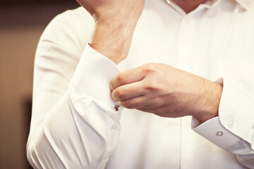 man fastens the cuffs on his white shirt. Close