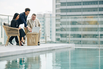 Group of successful business people meeting on rooftop by swimming pool and discussing presentation...