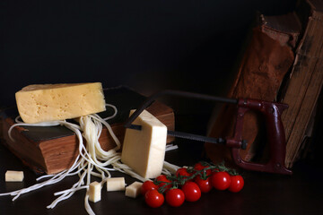 Still life with three cheeses, cherry tomatoes, old books and arm saw, absurd food photo