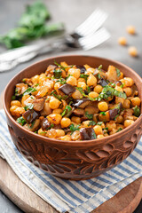 Cooked chickpeas with eggplant, parsley, olive oil, garlic, and spices in a ceramic bowl close-up. Vegetarian food, Middle Eastern cuisine.