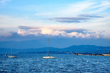 Lake at sunset with clouds and mountain profiles with sailboats.