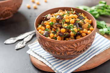 Cooked chickpeas with eggplant, parsley, olive oil, garlic, and spices in a ceramic bowl close-up. Vegetarian food, Middle Eastern cuisine.