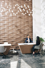 Serious mixed-race entrepreneur conducting job interview with young female applicant in modern office