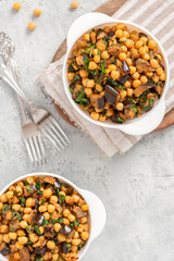Cooked chickpeas with eggplant, parsley, olive oil, garlic, and spices in a white bowl on a grey background top view. Vegetarian food, Middle Eastern cuisine.