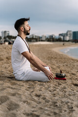 Young man meditating and singing om mantra in the beach