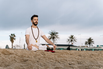 Fototapeta na wymiar Enlightened man with beard practicing meditation exercises on the beach at dawn