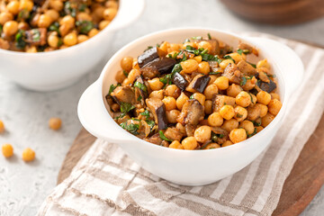 Cooked chickpeas with eggplant, parsley, olive oil, garlic, and spices in a white bowl close-up. Vegetarian food, Middle Eastern cuisine.