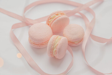 Lots of delicate French macaroons lie on a white background with a pink ribbon. Vintage. Advertising. Desser. Postcard. Place for an inscription. View from above. Dessert with tea. Confectioner.
