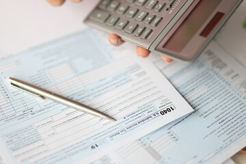 Naklejka na ściany i meble Hand holding calculator over tax form document closeup