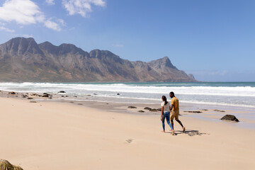 Obraz premium African american couple walking holding hands on a beach by the sea