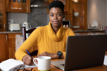 Fototapeta na wymiar Portrait of african american woman wearing earphones taking notes while working from home