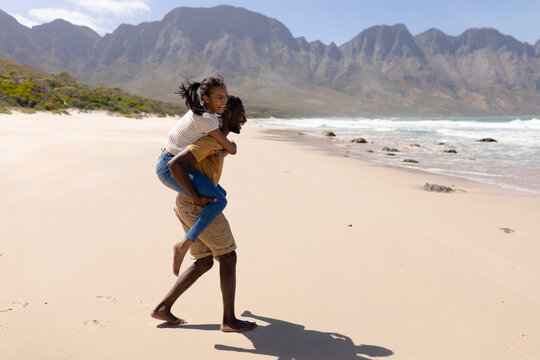 African american couple having fun piggybacking on a beach by the sea
