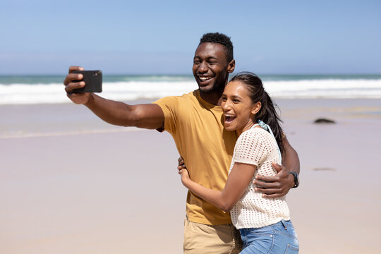 African american couple taking a selfie with smartphone on a beach by the sea - Powered by Adobe