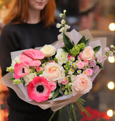 Big beautiful bouquet of different bright colorful flowers in hand of woman in beige apron.