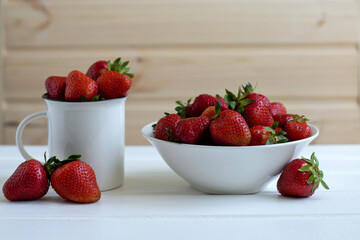 red juicy ripe strawberries in a white dish on a white wooden background, berries, vitamins, space for text