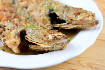 Thai Giant gourami fish and garlics deep fried and sweet spicy sauce in white dish on pine wooden table. Deep fried fish with Sweet chili. Thai food fried fish with spicy sauce. Thai style food.