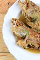 Thai Giant gourami fish and garlics deep fried and sweet spicy sauce in white dish on pine wooden table. Deep fried fish with Sweet chili. Thai food fried fish with spicy sauce. Thai style food.