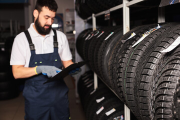 Fototapeta na wymiar confident meachanic man during work, focus on tires at the repair garage. replacement of winter and summer tires. seasonal tire replacement concept.