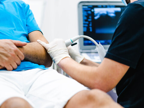Unrecognizable medical practitioner in latex gloves examining arm of crop male patient with ultrasound equipment in modern hospital