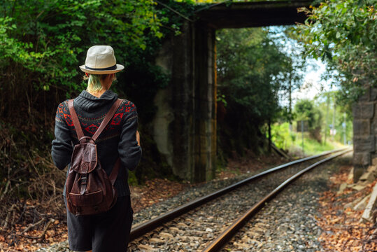Back view of female traveler with backpack standing on rails in forest during summer adventure