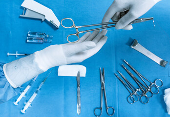 Top view of crop hand of anonymous assistant passing medical scissors to surgeon over table with various professional tools and instruments during operation in hospital
