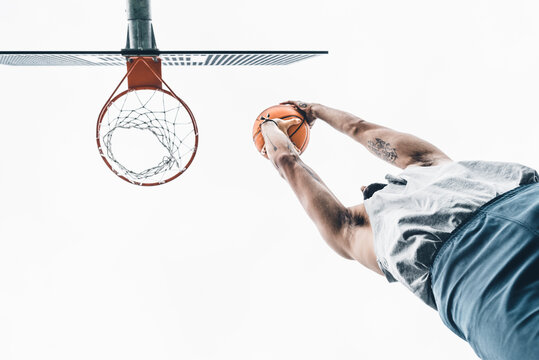 From below of unrecognizable sporty male throwing basketball ball into hoop while playing game on street sports ground
