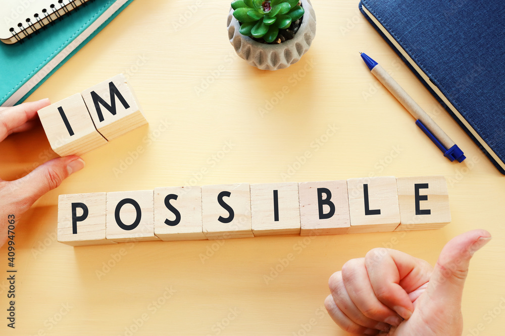 Poster man hand holding wooden cubes with the text impossible, removing the word im so it written possible.