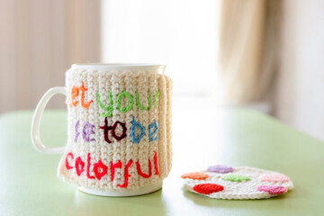 White mug for hot drinks, decorated with a knitted jacket with an inscription.