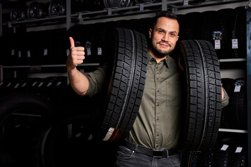 Fototapeta na wymiar male customer is satisfied with purchase of tyre in automobile repair garage, stand holding rubber for car in hands,in auto store shop