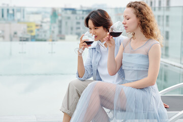 Multi-ethnic girlfriends drinking red wine when having romantic date on rooftop