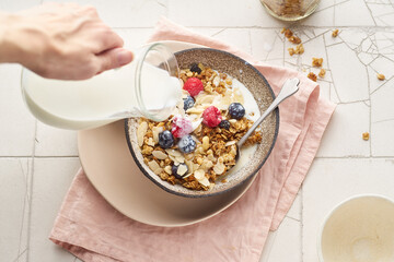 Hand with a jug pouring milk to granola with berries
