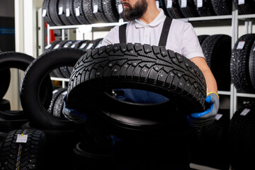car mechanic in a workshop on a stack of tires at his workplace, young male in uniform holding tire in hands © alfa27