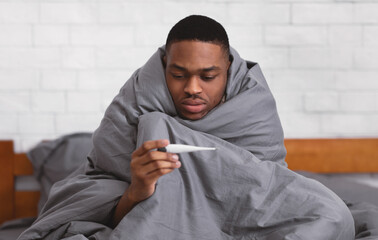 Ill Black Man Holding Thermometer Sitting Wrapped In Blanket Indoors