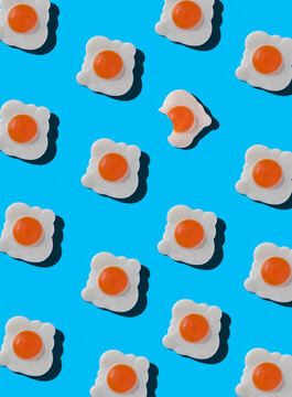 Top view of pattern of whole sweet candies in shape of fried eggs with one bitten arranged on blue background