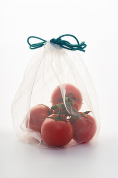 Still life with tomatoes in net mesh bag back lit on white background
