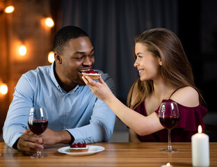 Romantic interracial couple having dinner date in restaurant, feeding each other