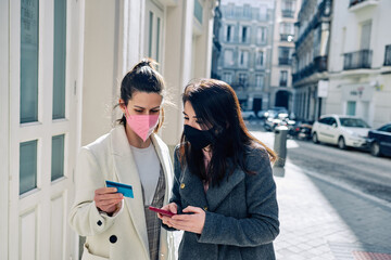 Two women shopping with their credit card and using the phone.