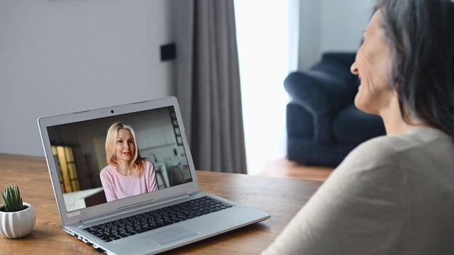 Two senior female friends has online meeting on the laptop, back view a senior woman talking via video call with her mate, employee, coworker, waving into webcam. Virtual conference concept