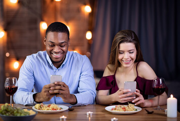 Phubbing. Young Interracial Couple Looking At Their Smartphones At Date In Restaurant