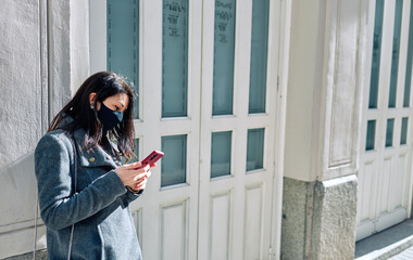 Woman waiting in the street with face mask on and her phone.