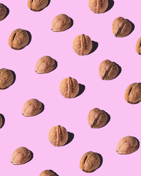 From above of brown walnuts arranged in rows on pink background in studio