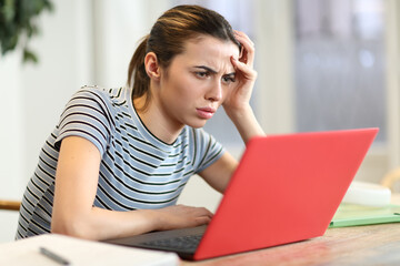 Worried woman checking red laptop at home