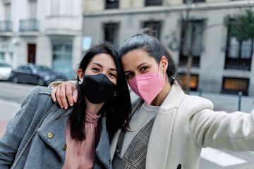 Two women taking a selfie in the street with their face masks on.