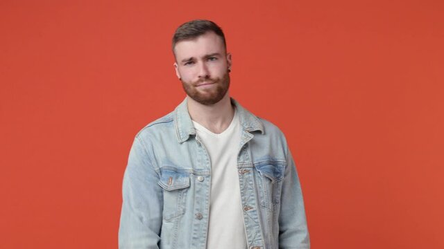Confused bearded young man 20s in casual white t-shirt denim jacket isolated on orange background studio. People lifestyle concept. Point index finger himself ask say who me no thanks i do not need it