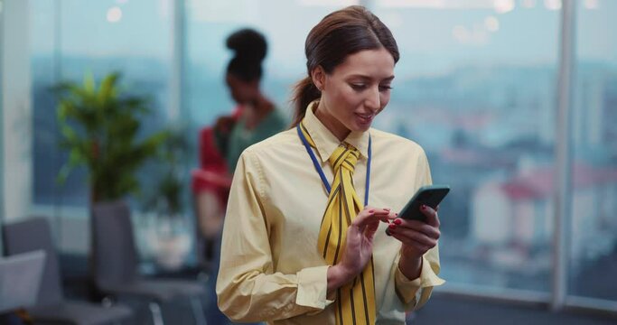 Attractive young stewardess using smartphone online application texting message to crew standing in waiting room. Airport personnel. Terminal.