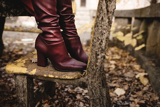 Side view of crop anonymous female in stylish elegant leather boots standing on old stone bench in autumn park