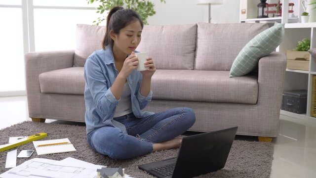 Asian professional woman worker sitting with tool and paper while running program on pc and checking data on the layout at home workday.