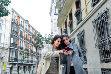Two women using their smartphones in the street.